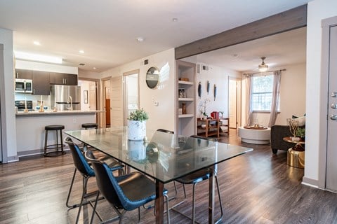 a dining area with a glass table and chairs and a kitchen in the background